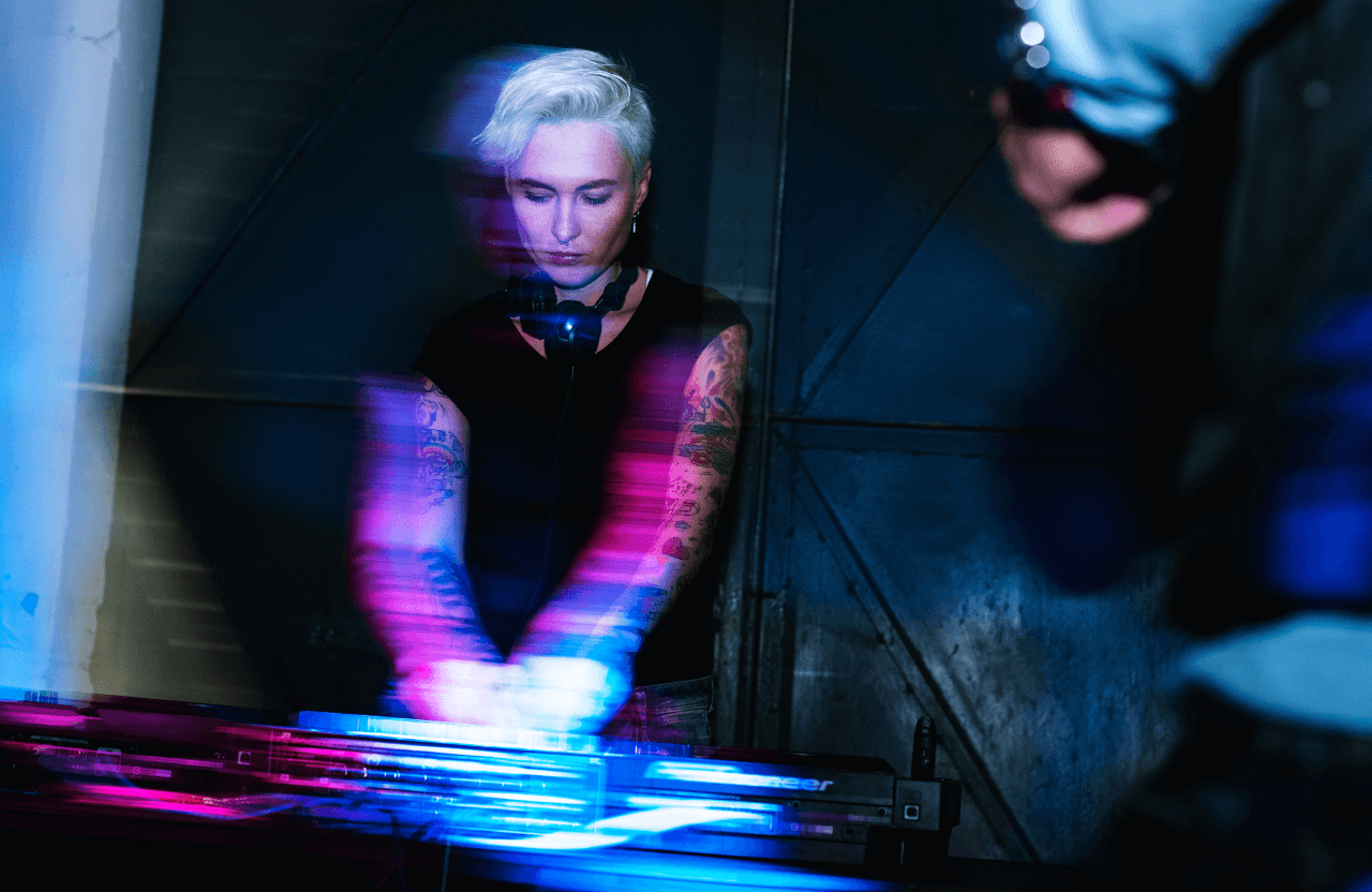 FX Productions Canada A DJ with short white hair and tattoos mixes music on a console, surrounded by colorful motion blur and lighting effects in a dimly lit room, brought to life by Toronto Production Company. Toronto Video Production Company