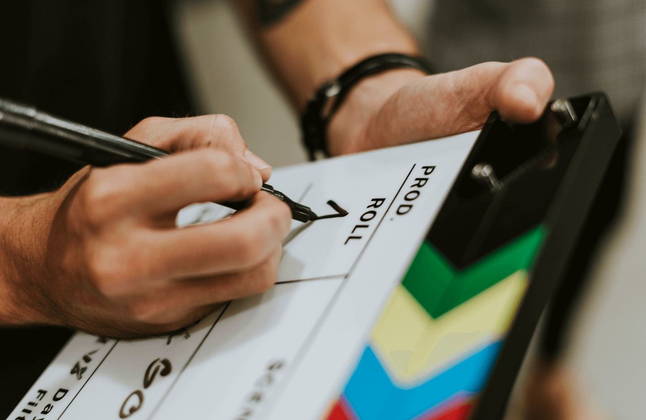 FX Productions Canada A person writes on a film clapperboard with a black marker, preparing it for a scene; colorful stripes line the side, showcasing the professional touch of FX Productions Canada. Toronto Video Production Company