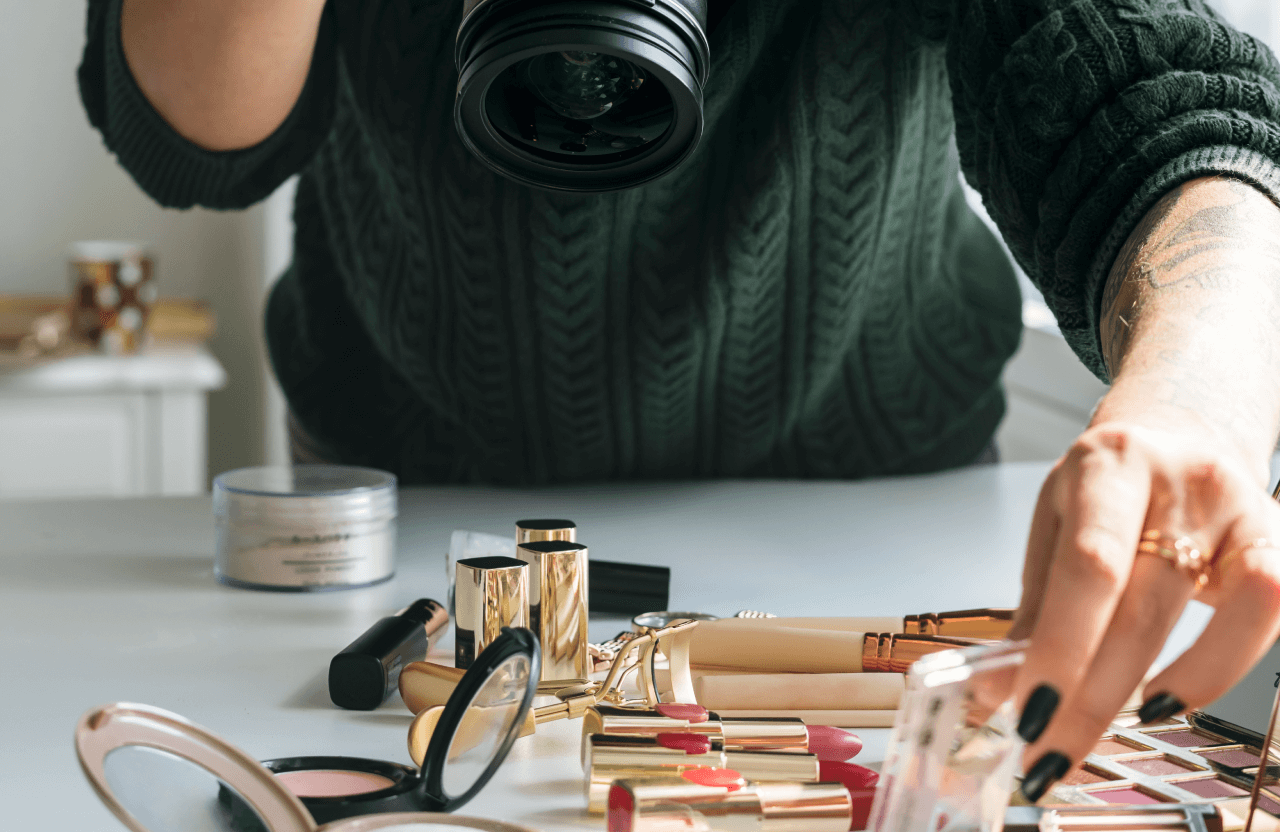FX Productions Canada A person in a dark green sweater takes photos of makeup products—lipsticks, powders, and palettes—neatly arranged on a white table for FX Productions Canada, a leading Toronto Production Company. Toronto Video Production Company