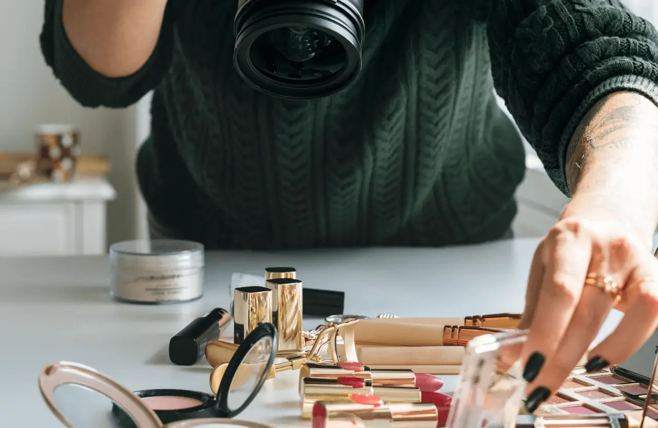 FX Productions Canada A person in a dark green sweater takes photos of makeup products—lipsticks, powders, and palettes—neatly arranged on a white table for FX Productions Canada, a leading Toronto Production Company. Toronto Video Production Company