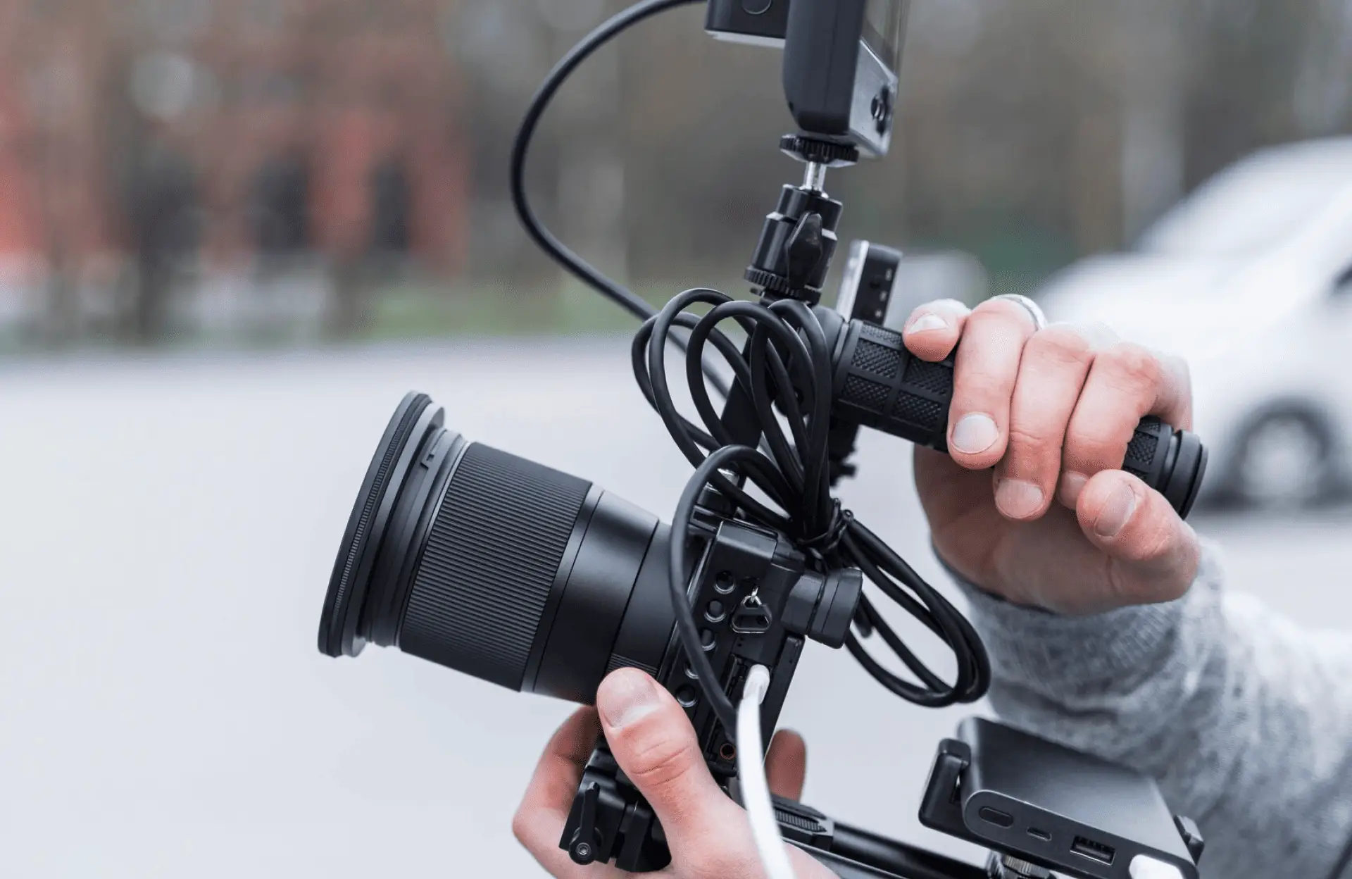 FX Productions Canada Close-up of a person holding a professional video camera with external monitor, cables, and accessories attached, outdoors. Toronto Video Production Company
