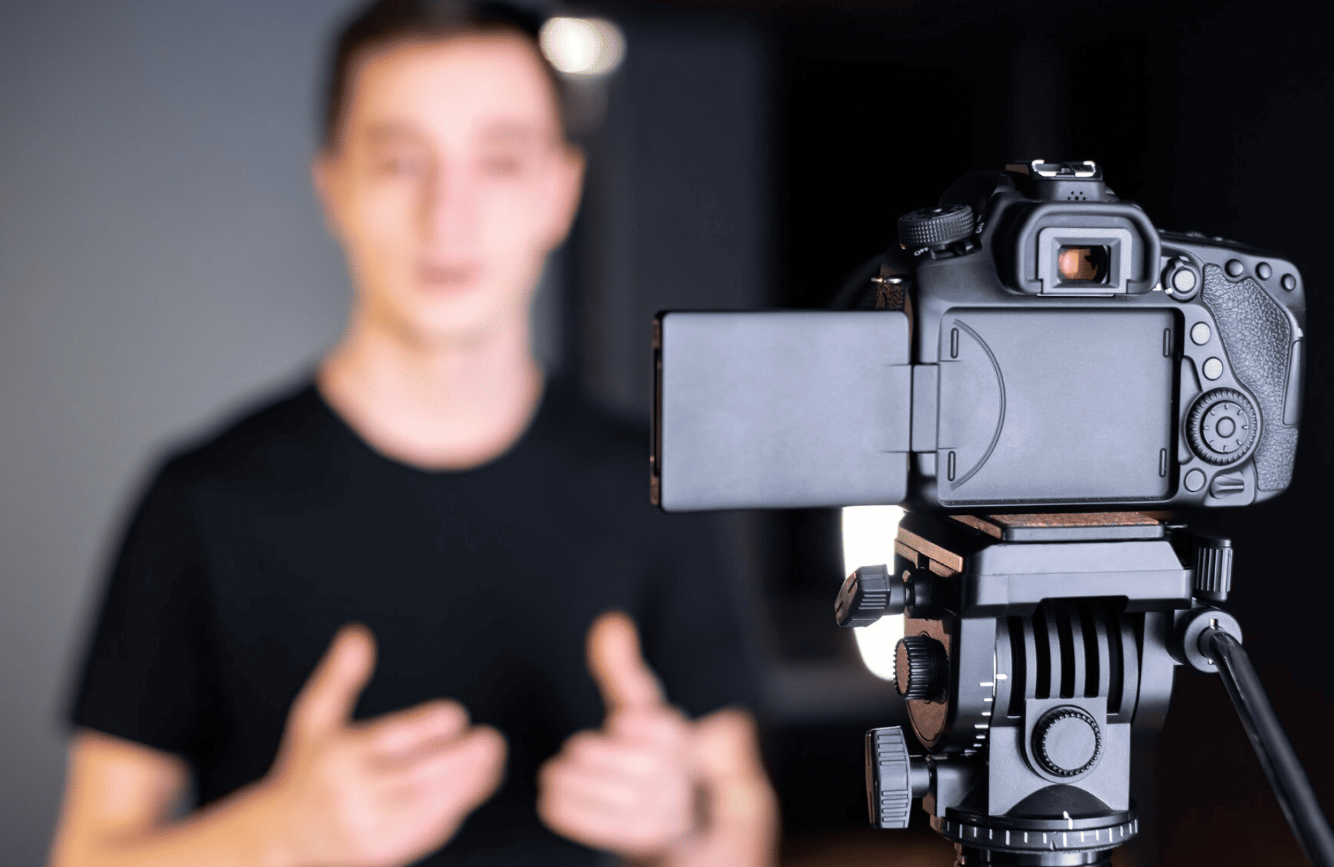 FX Productions Canada A digital camera on a tripod records a person in a black shirt speaking with hand gestures, who appears out of focus in the background. Toronto Video Production Company