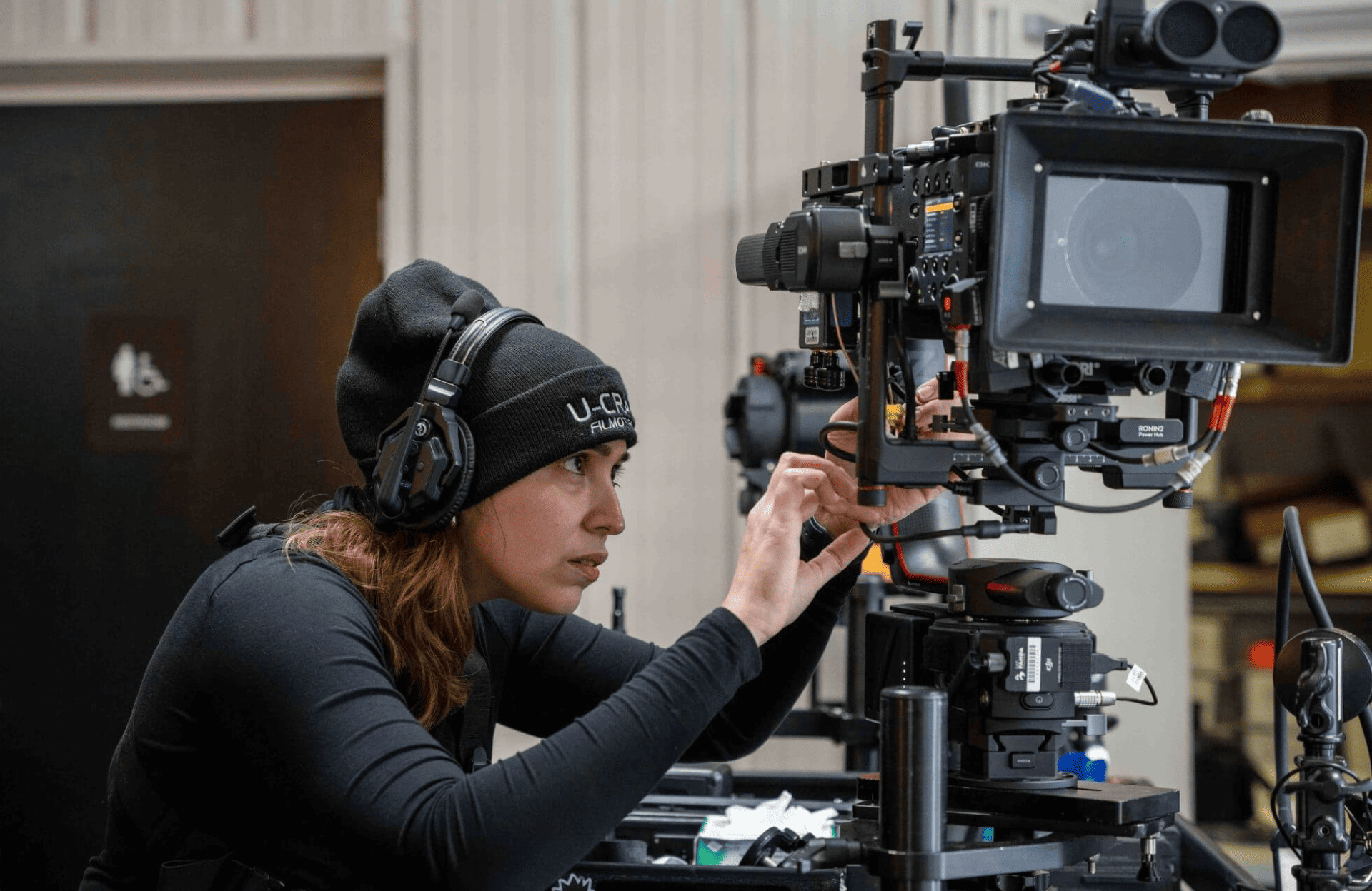 FX Productions Canada A person wearing headphones and a beanie adjusts a professional video camera on a tripod indoors, showcasing the behind-the-scenes expertise of FX Productions Canada. Toronto Video Production Company