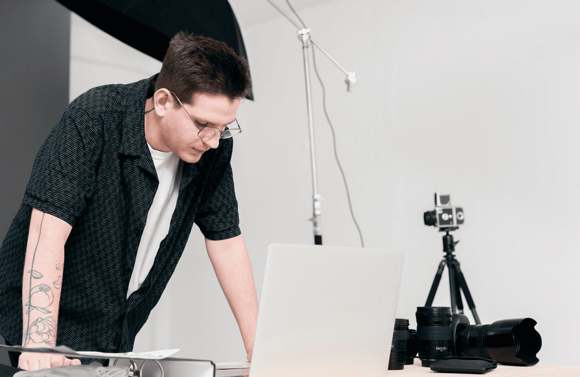 FX Productions Canada A person with glasses leans over a laptop on a desk with camera equipment, in a studio setting with a white wall and photography lights visible. Toronto Video Production Company