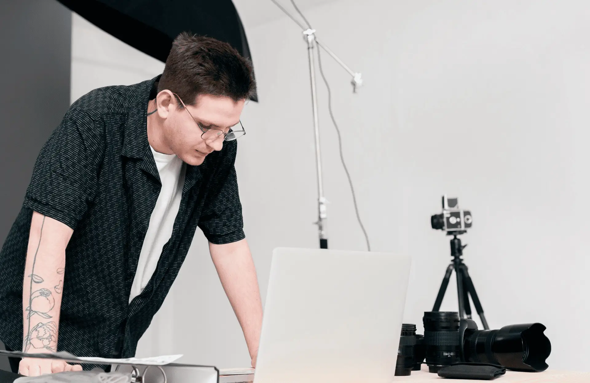 FX Productions Canada A person with glasses leans over a laptop on a desk with camera equipment, in a studio setting with a white wall and photography lights visible. Toronto Video Production Company