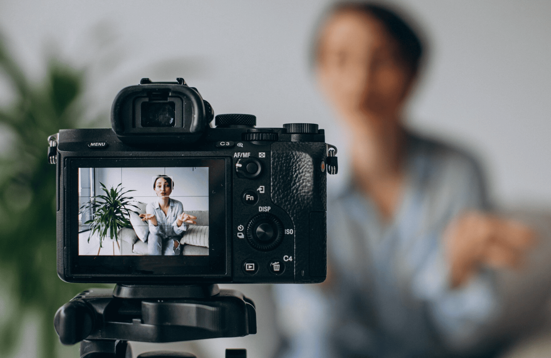 FX Productions Canada A camera on a tripod records a person speaking indoors, with the person and a plant visible on the camera’s screen in the foreground. Toronto Video Production Company