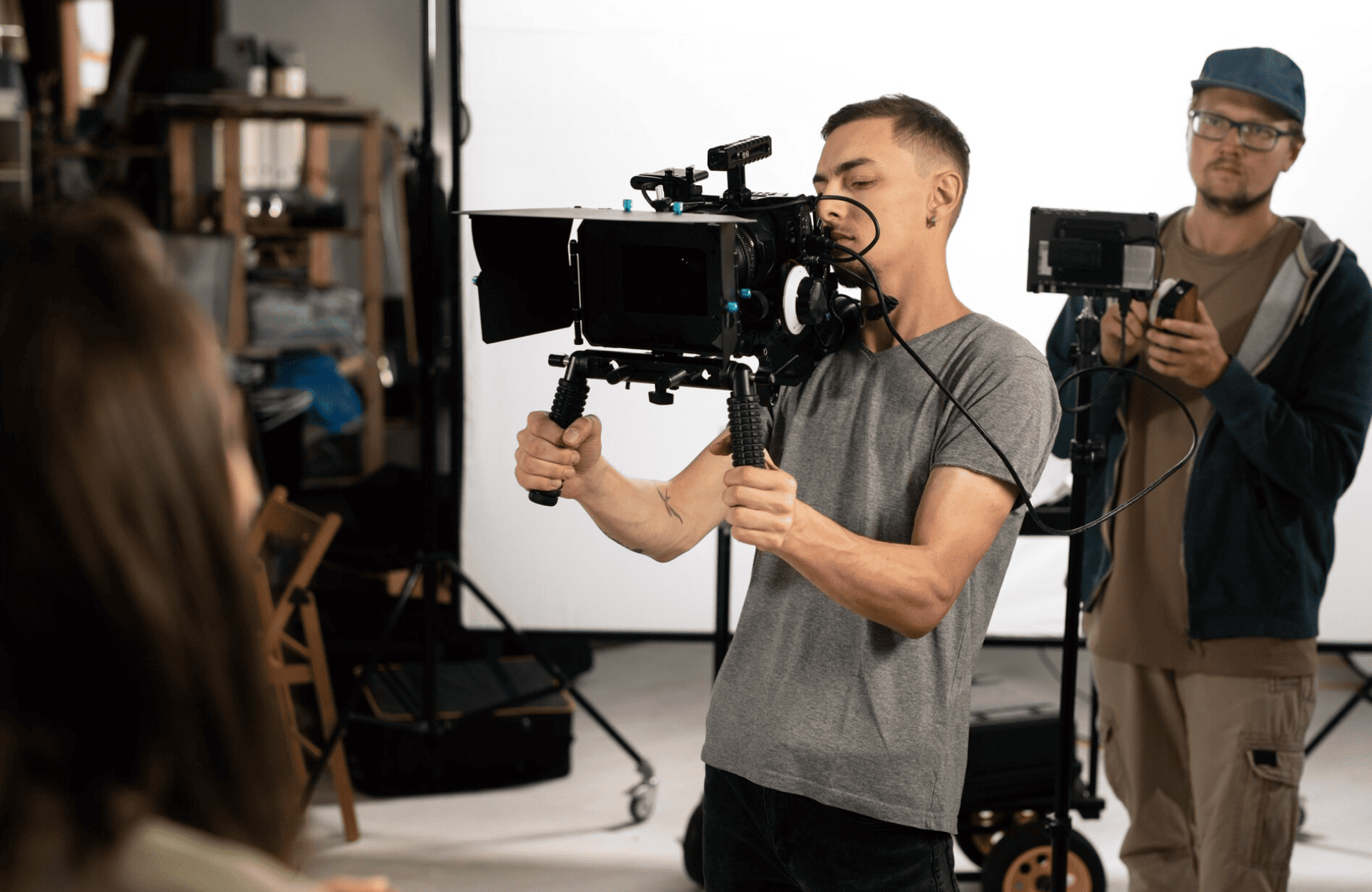 FX Productions Canada Two people operate cameras and filming equipment on a studio set; one holds a handheld camera rig, while the other monitors a video screen in the background. Toronto Video Production Company