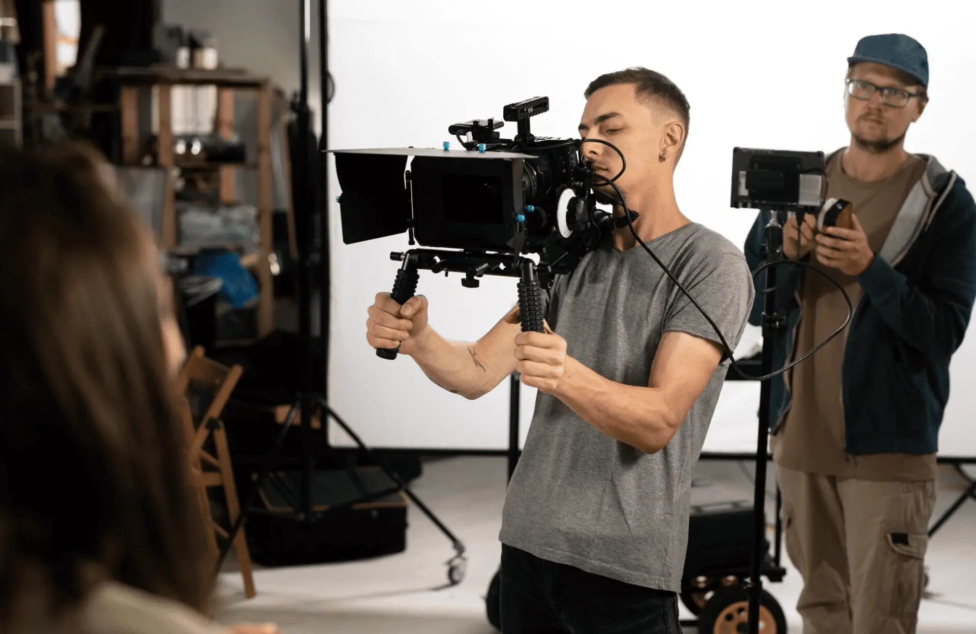 FX Productions Canada Two people operate cameras and filming equipment on a studio set; one holds a handheld camera rig, while the other monitors a video screen in the background. Toronto Video Production Company