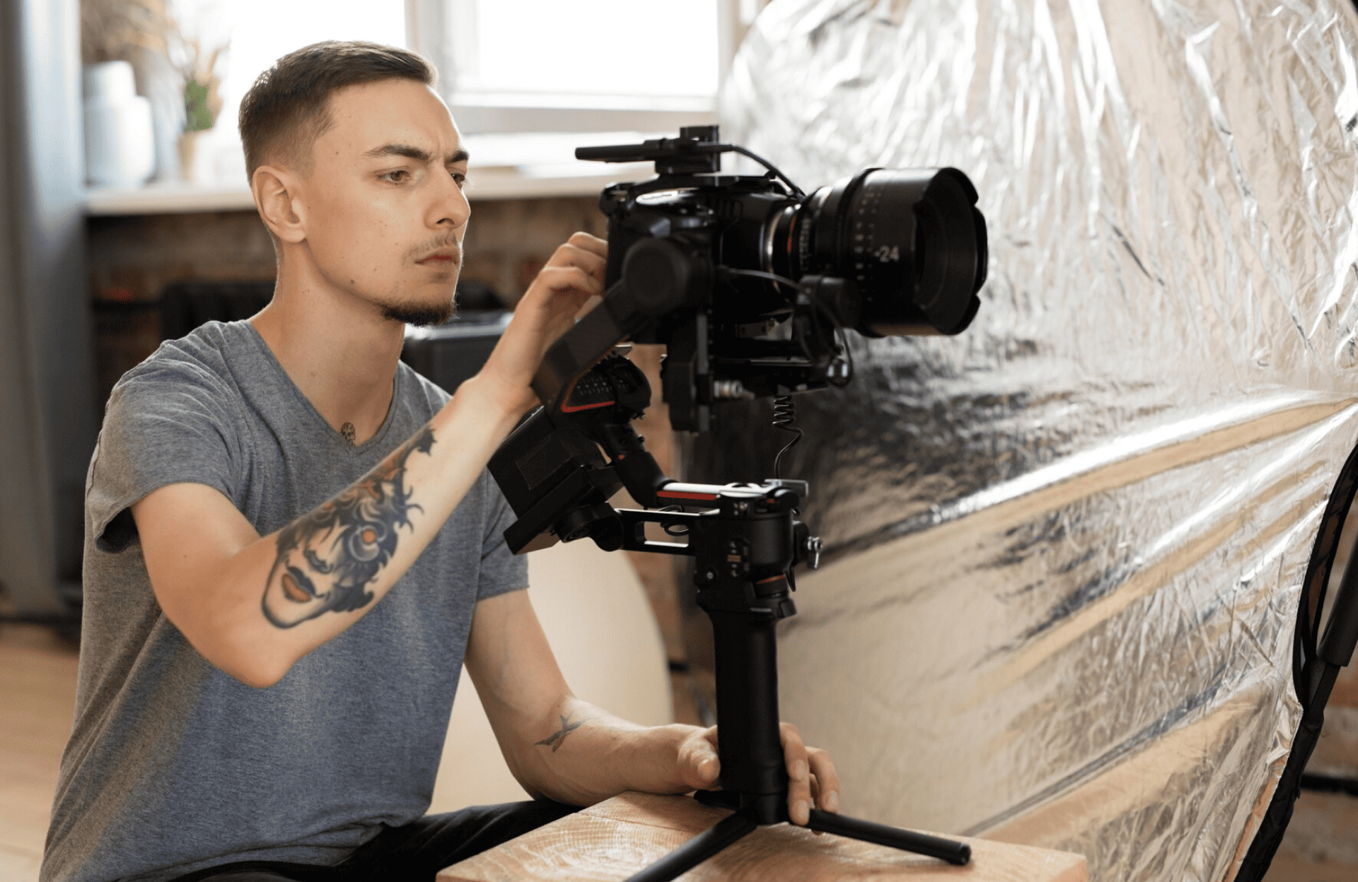 FX Productions Canada A man with a tattoo on his left arm operates a professional video camera mounted on a tripod indoors, with reflective material in the background. Toronto Video Production Company
