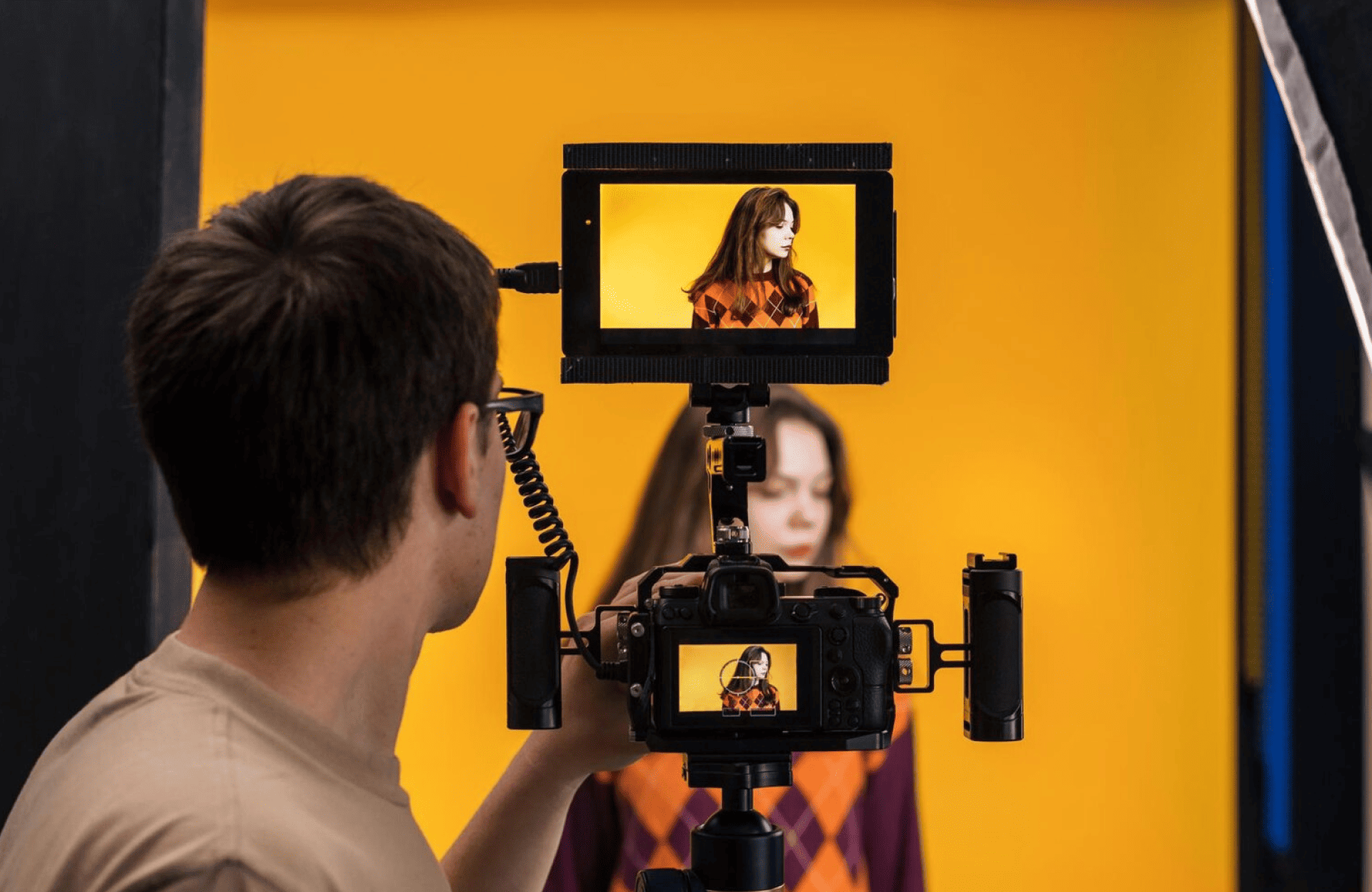FX Productions Canada A person films a woman standing against a yellow background, with her image visible on the camera monitor and a screen above. Toronto Video Production Company