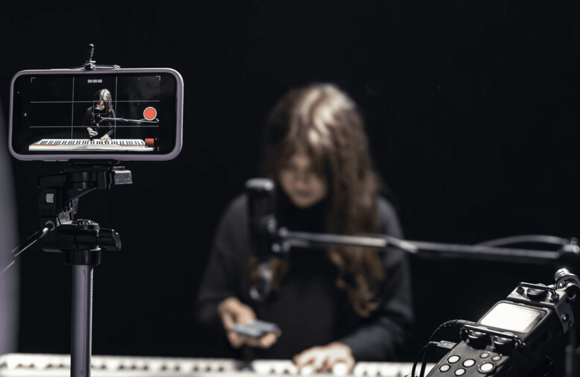 FX Productions Canada A person plays keyboard in a recording studio, filmed by a smartphone mounted on a tripod in the foreground. Toronto Video Production Company High-impact music videos