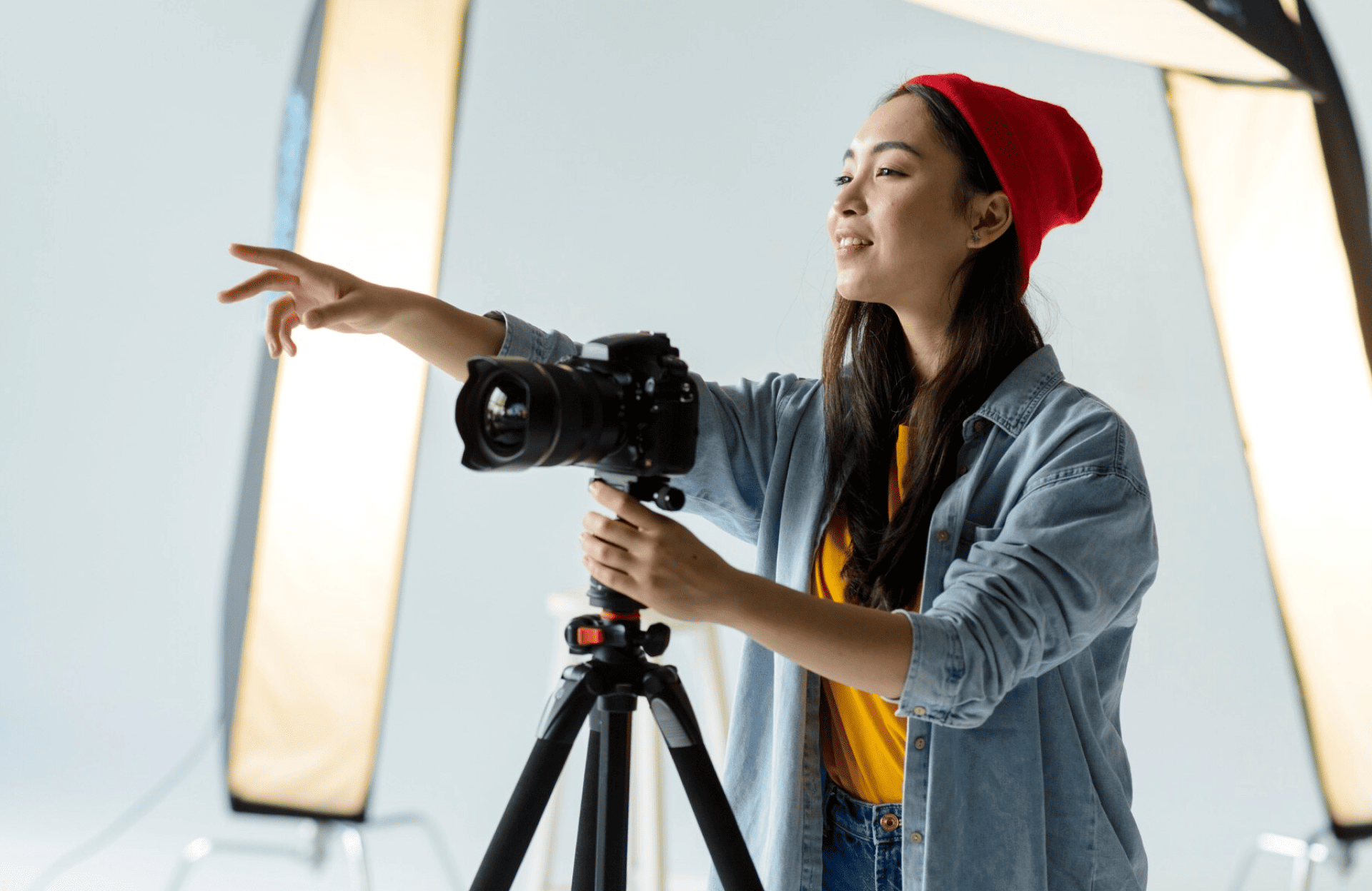 FX Productions Canada A woman wearing a red beanie adjusts a camera on a tripod and points while standing in a photography studio with softbox lights. Toronto Video Production Company
