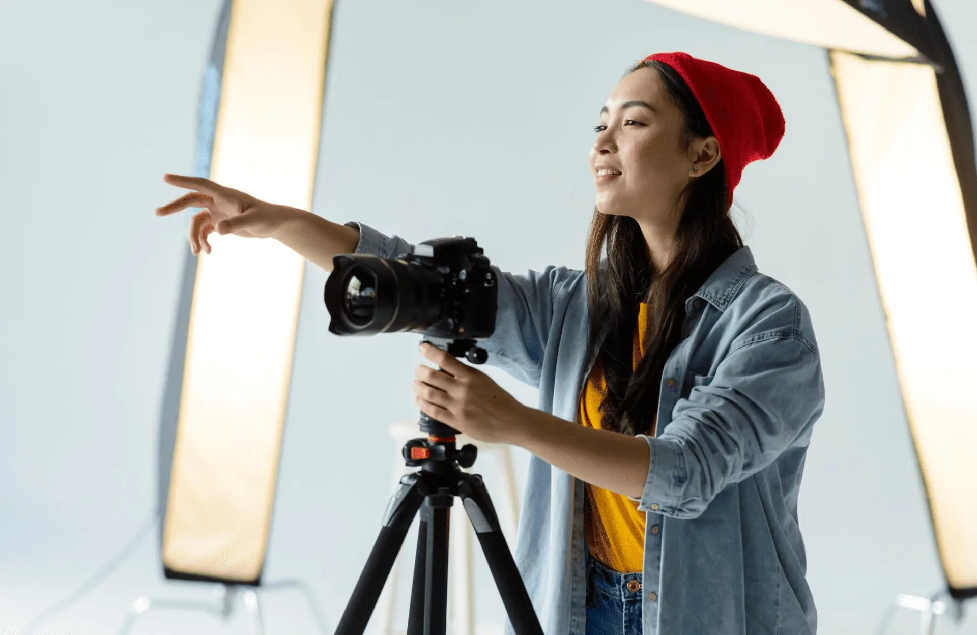 FX Productions Canada A woman wearing a red beanie adjusts a camera on a tripod and points while standing in a photography studio with softbox lights. Toronto Video Production Company