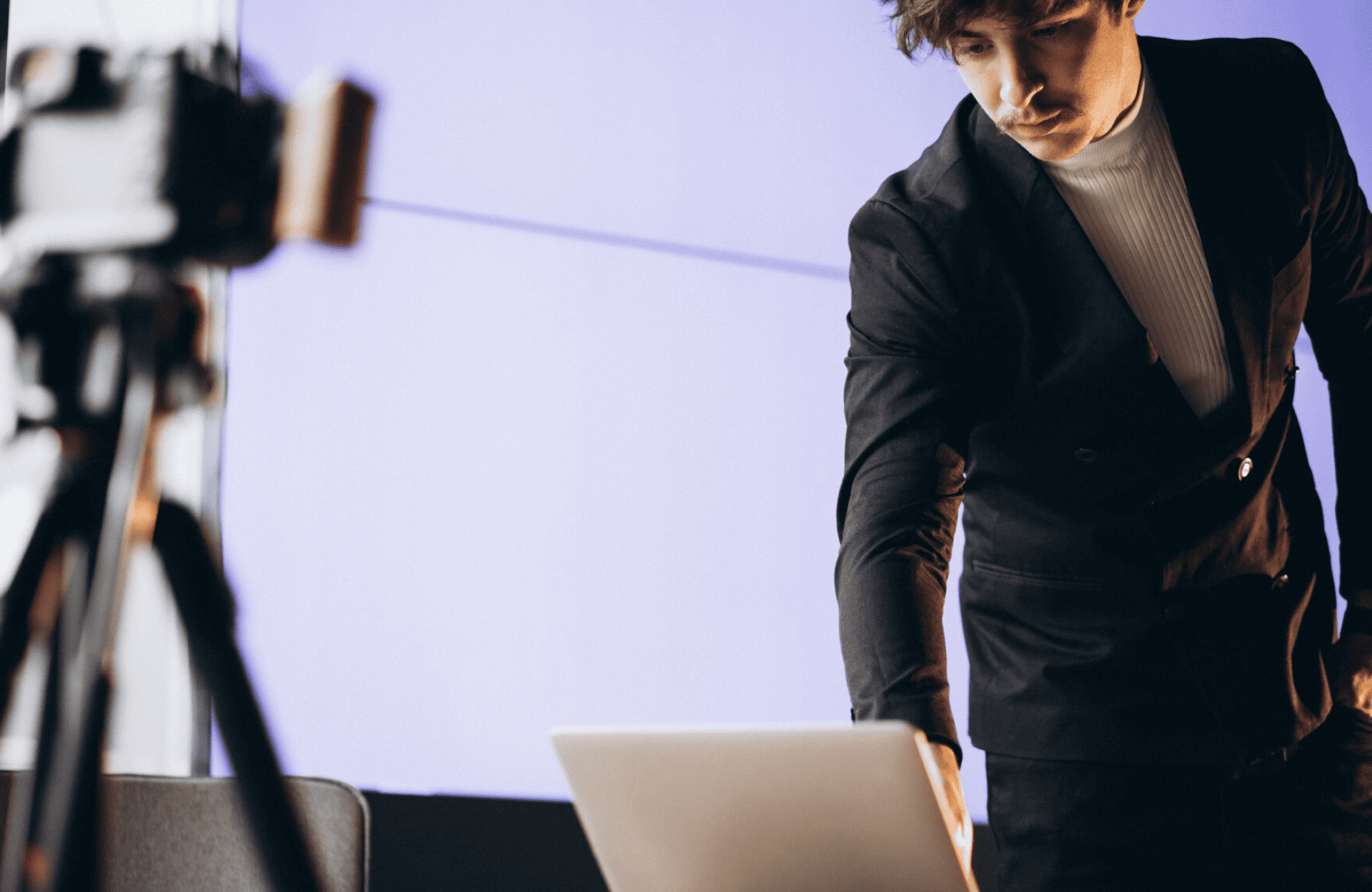 FX Productions Canada Man in a suit standing next to a laptop, reaching toward the keyboard, with a camera on a tripod in the foreground. Toronto Video Production Company