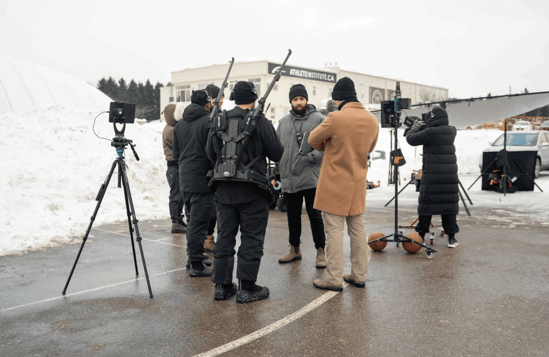 FX Productions Canada A film crew stands outside on a snowy lot with cameras, tripods, and sound equipment, preparing for a shoot near a building. Toronto Video Production Company