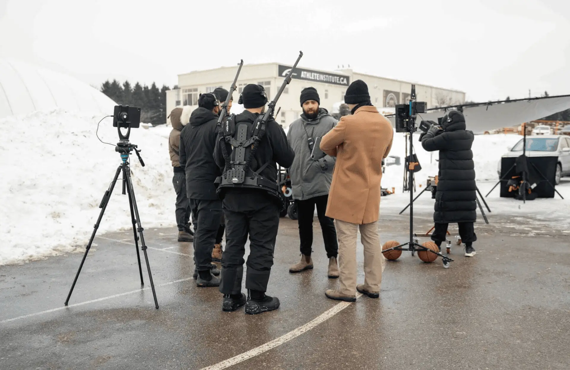 FX Productions Canada A film crew stands outside on a snowy lot with cameras, tripods, and sound equipment, preparing for a shoot near a building. Toronto Video Production Company
