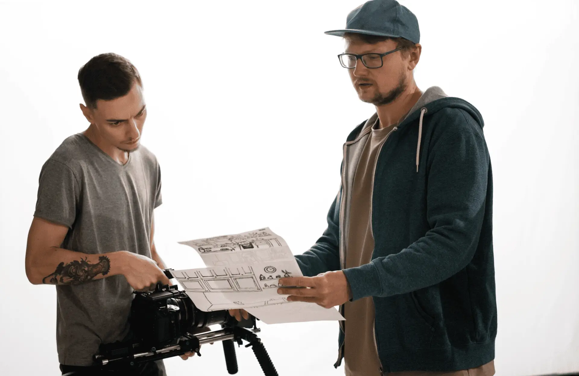 FX Productions Canada Two men stand together; one adjusts a camera on a tripod while the other holds and examines a storyboard against a plain white background. Toronto Video Production Company