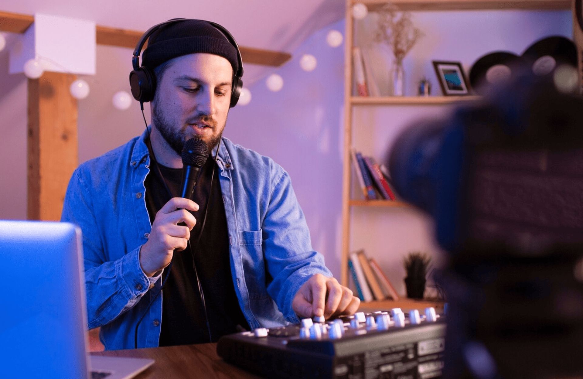 FX Productions Canada A man wearing headphones holds a microphone and adjusts audio equipment in front of a laptop, with a camera recording him in a room with shelves in the background. Toronto Video Production Company