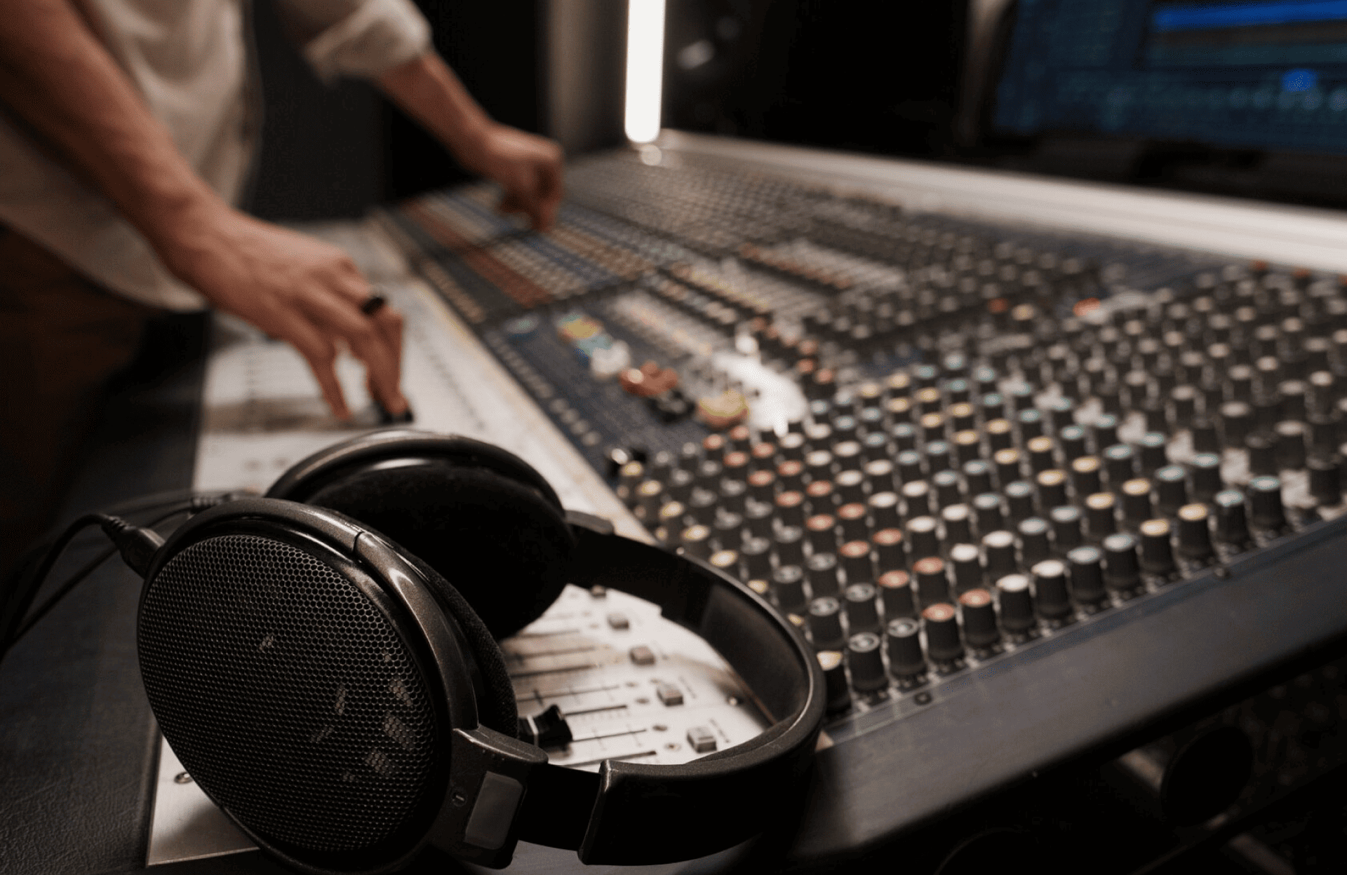 FX Productions Canada A close-up view of a large audio mixing console with headphones resting on it and a person adjusting the controls in the background. Toronto Video Production Company