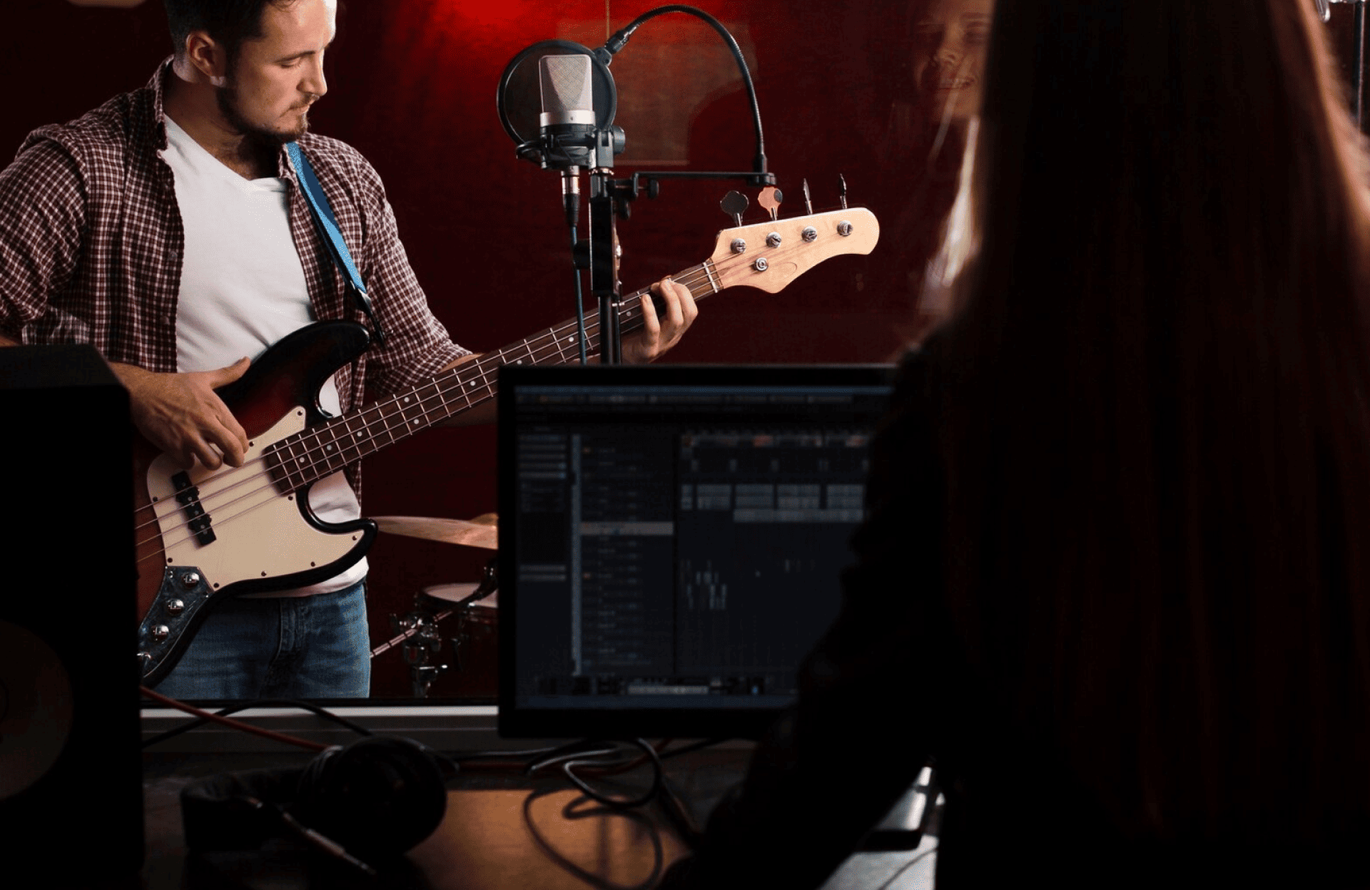 FX Productions Canada A musician plays an electric bass guitar in a recording studio while a person works at a computer mixing console in the foreground. Toronto Video Production Company