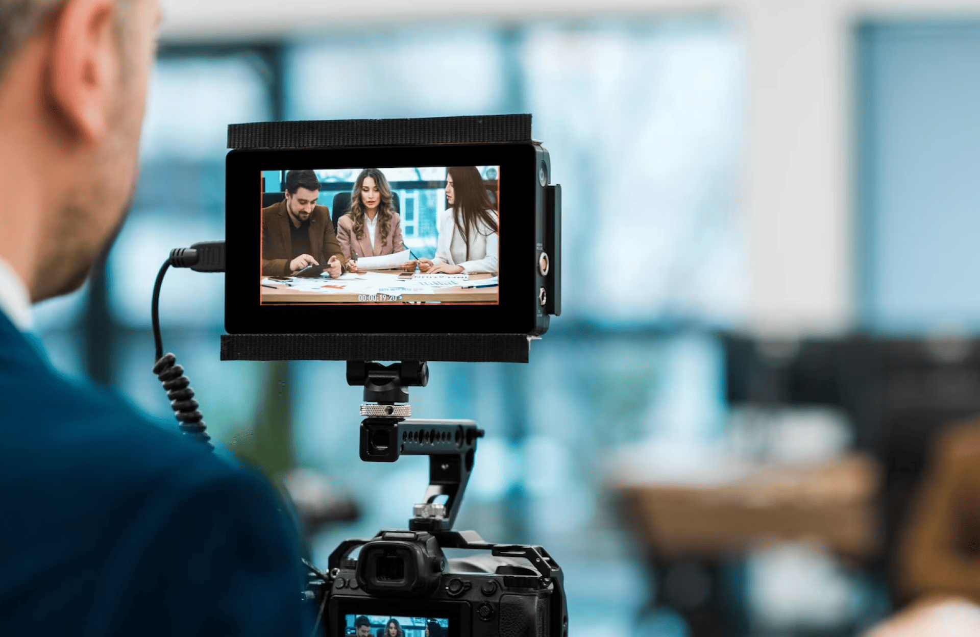 FX Productions Canada A camera films three people sitting at a table and discussing documents, as seen on the camera's display screen in a modern office setting. Toronto Video Production Company