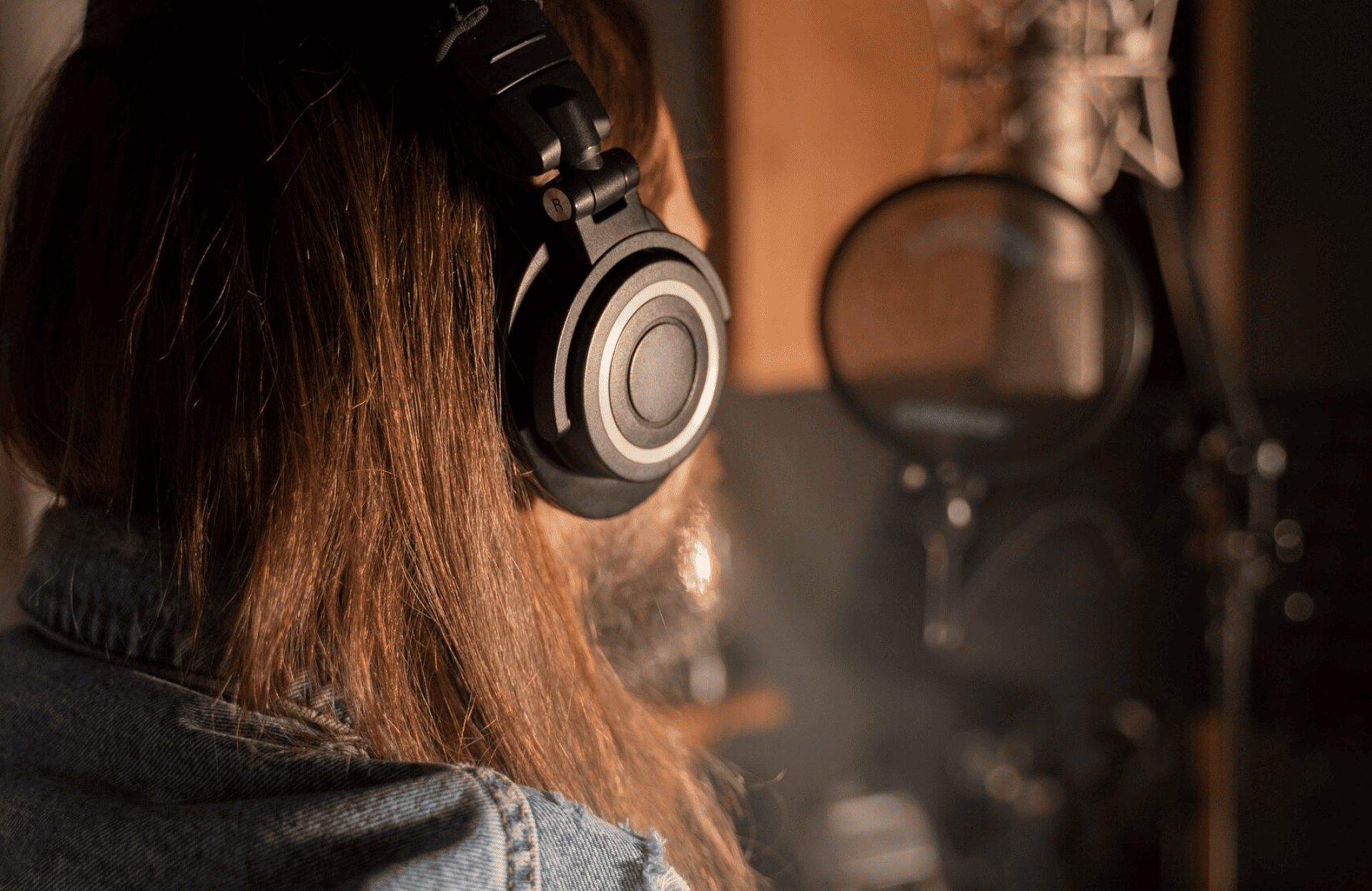 FX Productions Canada Person with long hair wearing headphones and a denim jacket is in front of a microphone in a recording studio. Toronto Video Production Company