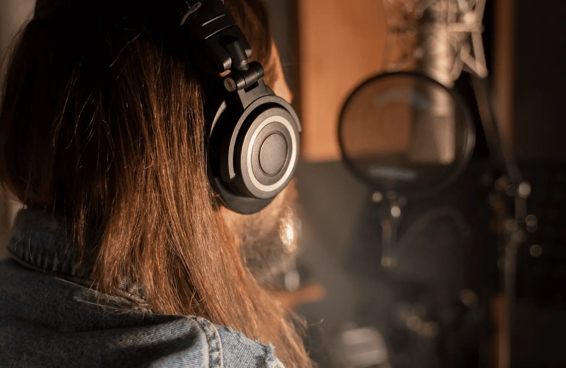 FX Productions Canada Person with long hair wearing headphones and a denim jacket is in front of a microphone in a recording studio. Toronto Video Production Company