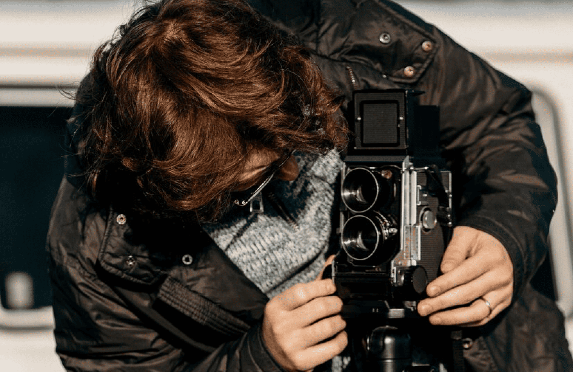 FX Productions Canada A person with curly hair adjusts a vintage twin-lens camera on a tripod outdoors, wearing a dark jacket and glasses. Toronto Video Production Company