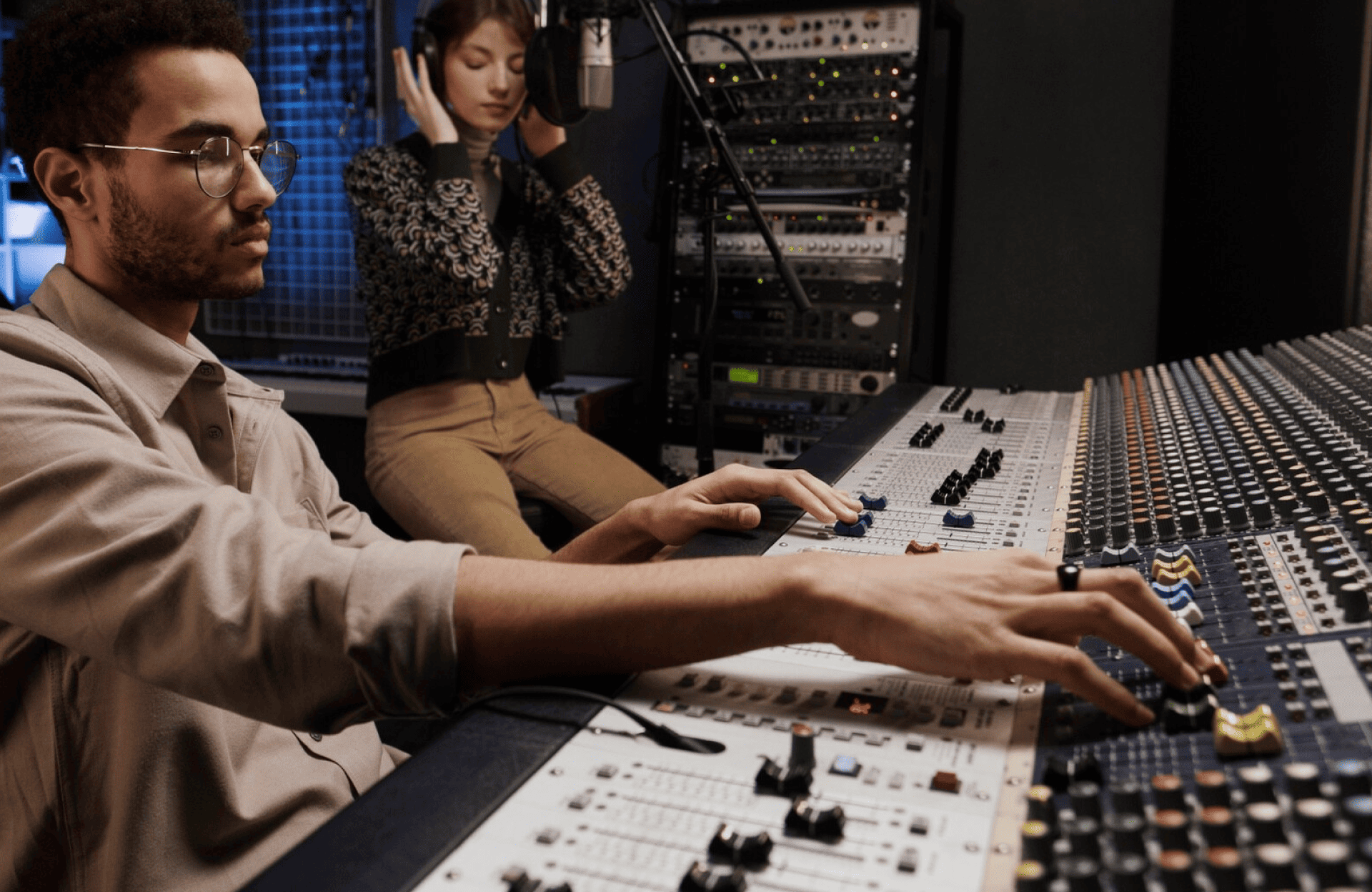 FX Productions Canada A man adjusts controls on a large audio mixing console while a woman stands behind him wearing headphones in a recording studio. Toronto Video Production Company