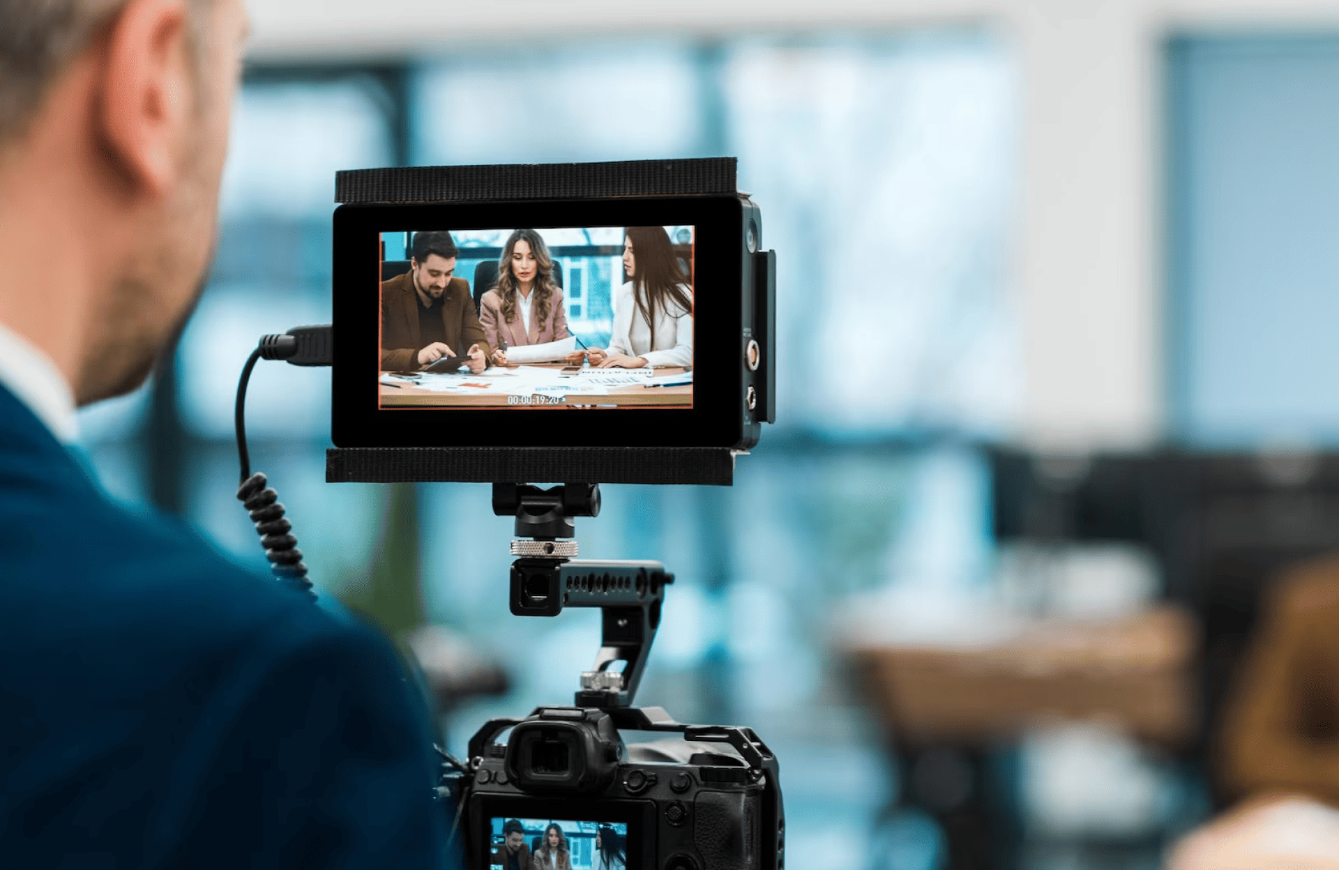 FX Productions Canada A camera films three people sitting at a table having a discussion, as seen through the camera’s display screen in an indoor office setting. Toronto Video Production Company