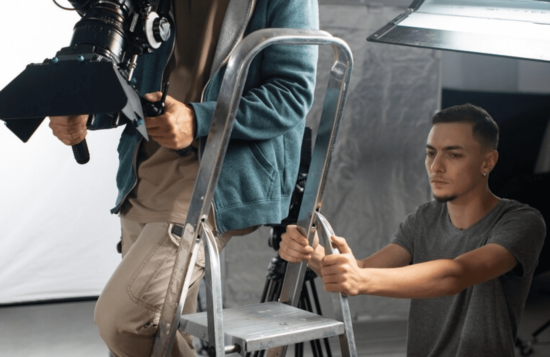 FX Productions Canada A person stands on a ladder operating a professional camera, while another person steadies the ladder on a film set. Toronto Video Production Company