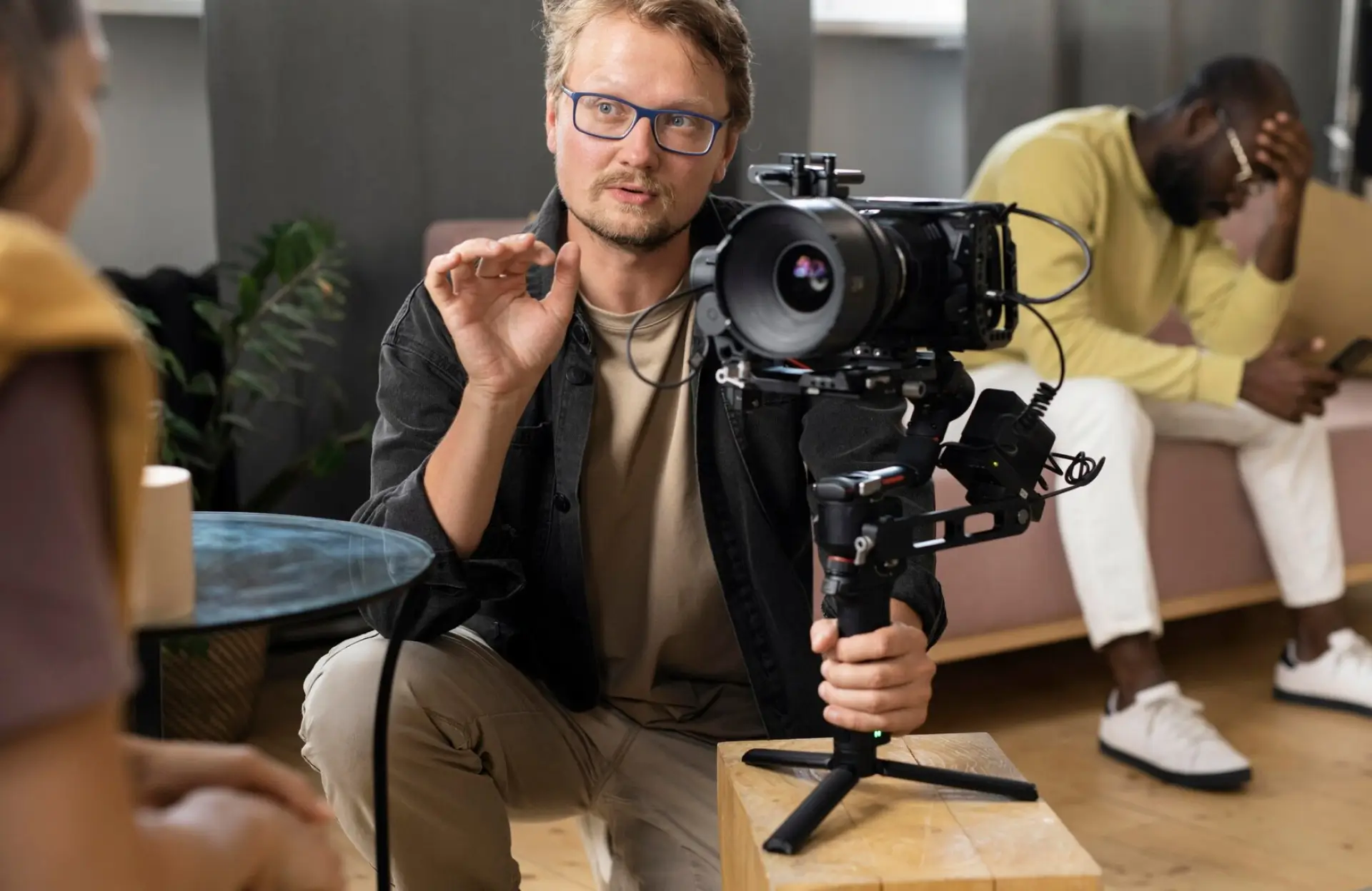 FX Productions Canada A person holding a professional video camera explains something to someone off-frame, while another person in the background looks down at a phone with their hand on their forehead. Toronto Video Production Company