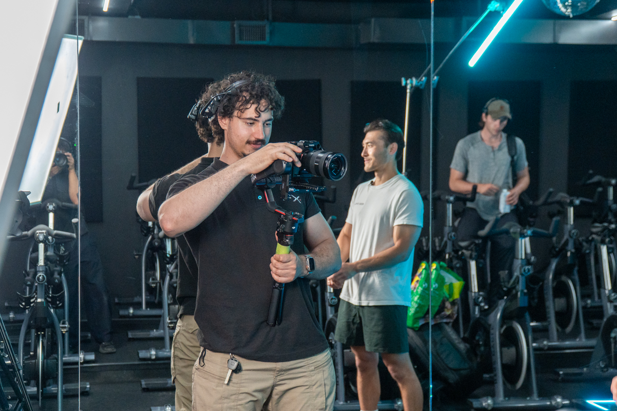 FX Productions Canada A person operates a camera on a stabilizer in a fitness studio, with two others standing nearby among stationary bikes. Toronto Video Production Company