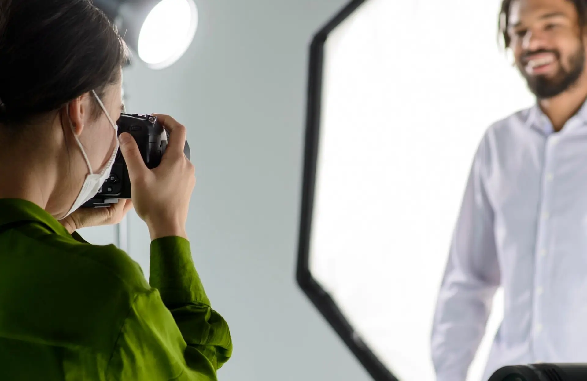 FX Productions Canada A photographer wearing a green shirt takes a photo of a smiling man in a white shirt in a well-lit studio with a large softbox in the background. Toronto Video Production Company