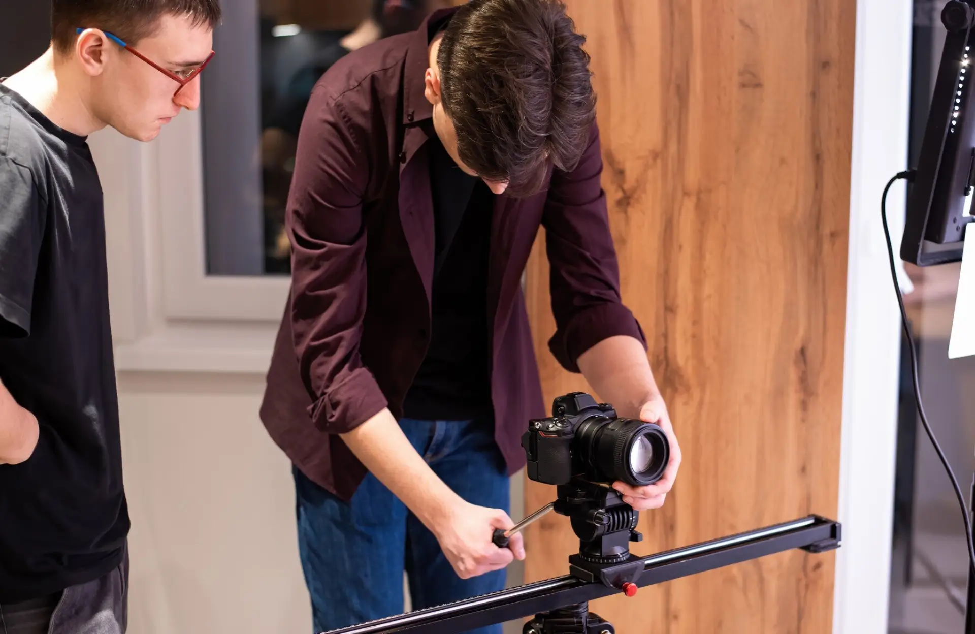 FX Productions Canada Two people adjust a camera mounted on a tripod slider indoors, focusing on setup and equipment handling. Toronto Video Production Company