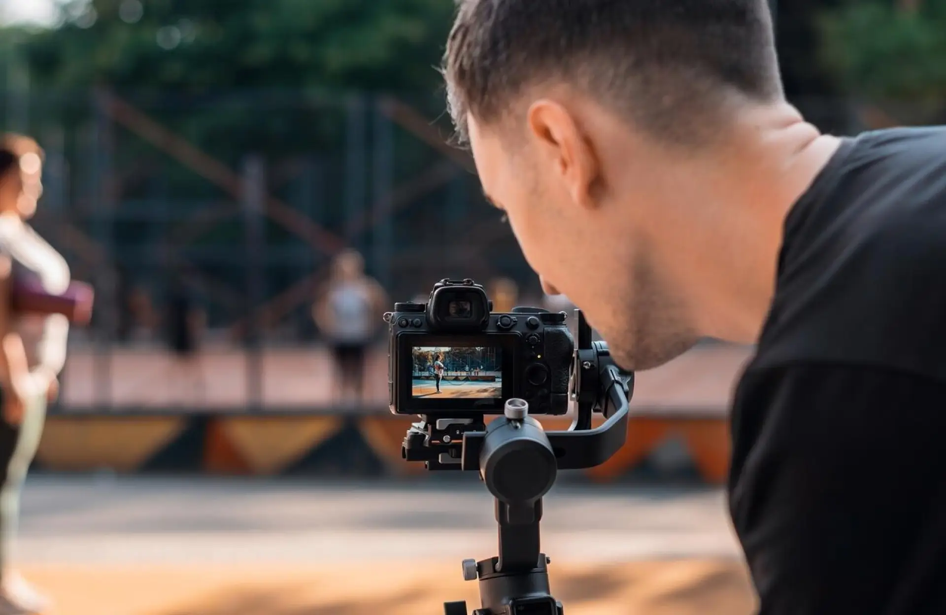 FX Productions Canada A person operates a camera mounted on a stabilizer, filming another person standing outdoors with blurred trees and a fence in the background. Toronto Video Production Company