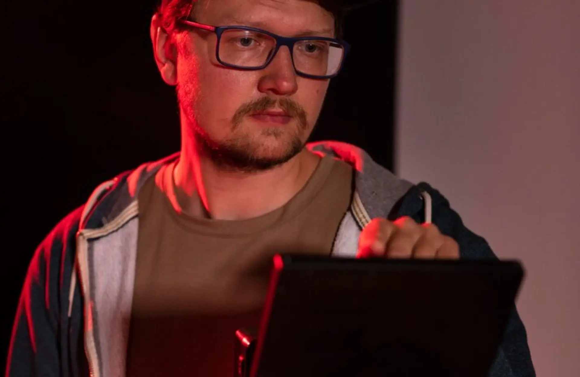 FX Productions Canada A man wearing glasses and a hoodie uses a digital tablet in a dimly lit setting with red lighting. Toronto Video Production Company