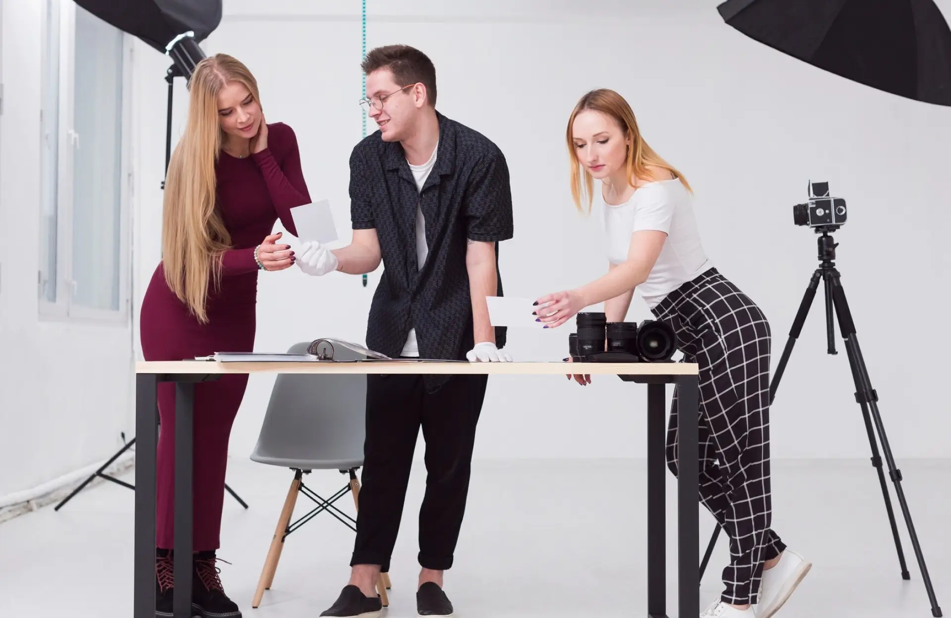 FX Productions Canada Three people wearing gloves examine photographs on a table in a photography studio, with cameras, lenses, and lighting equipment visible around them. Toronto Video Production Company