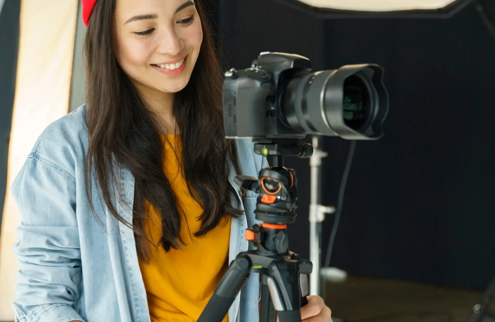 FX Productions Canada A woman wearing a red beanie and yellow shirt smiles while adjusting a camera mounted on a tripod in a studio setting. Toronto Video Production Company