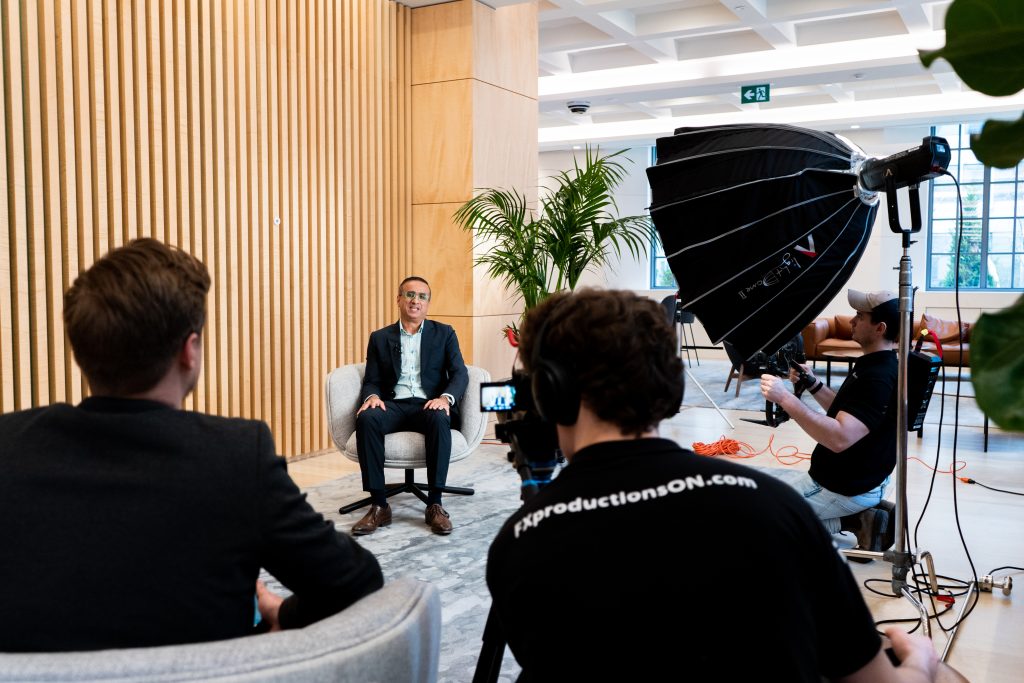 FX Productions Canada A man in a suit sits for an interview on camera, with a film crew recording him in a modern office space equipped with professional lighting. Toronto Video Production Company