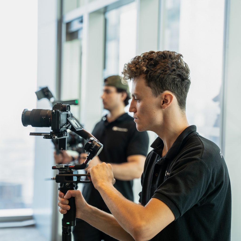 FX Productions Canada Two people in black polo shirts operate professional video cameras with stabilizers in a bright indoor setting with large windows. Toronto Video Production Company