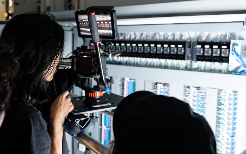 FX Productions Canada A person operates a camera to film an open electrical control panel filled with switches and wires. Toronto Video Production Company