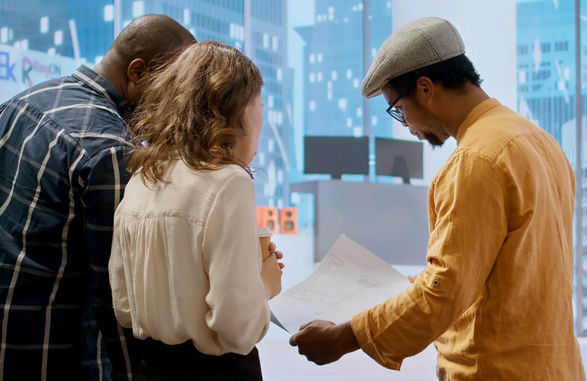 FX Productions Canada Three people stand together indoors, looking at architectural plans or drawings, with a cityscape image displayed in the background. Toronto Video Production Company