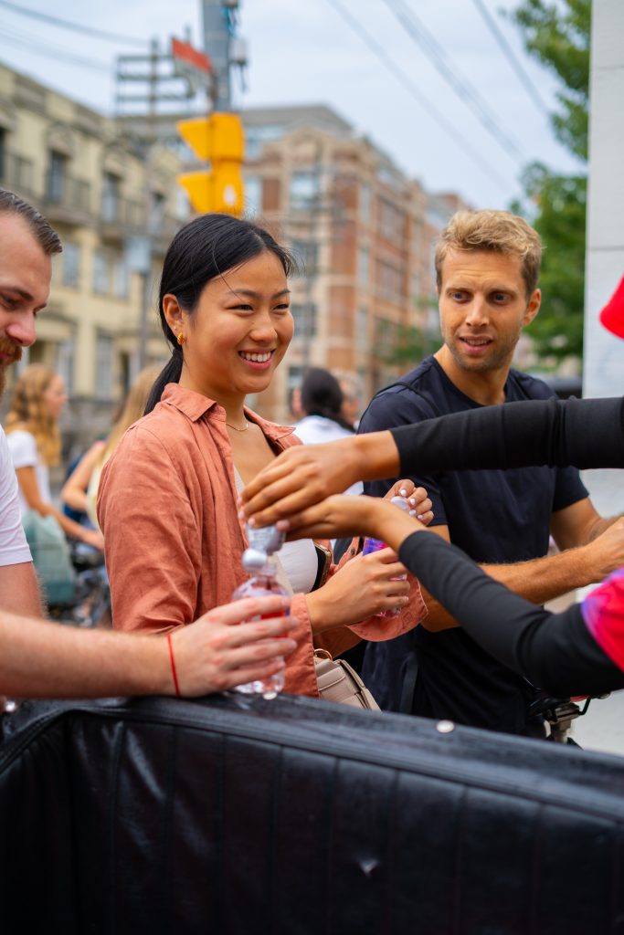 FX Productions Canada A woman and man receive water bottles from volunteers at an outdoor event in an urban area, with buildings and people visible in the background. Toronto Video Production Company