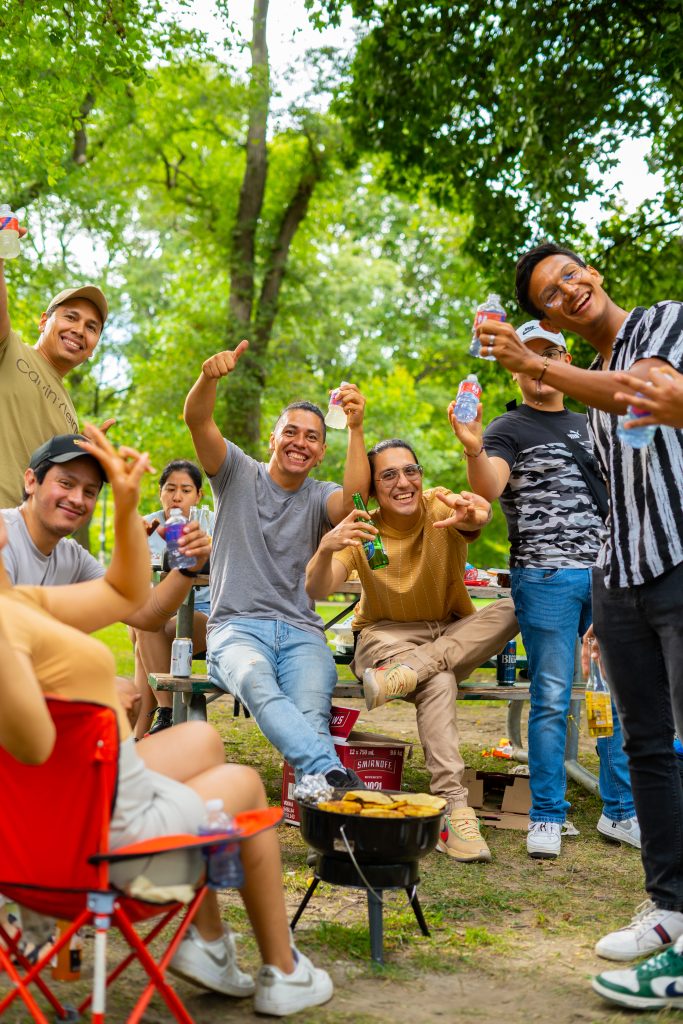 FX Productions Canada A group of people smiling and raising drinks around a small grill at an outdoor picnic in a park. Toronto Video Production Company