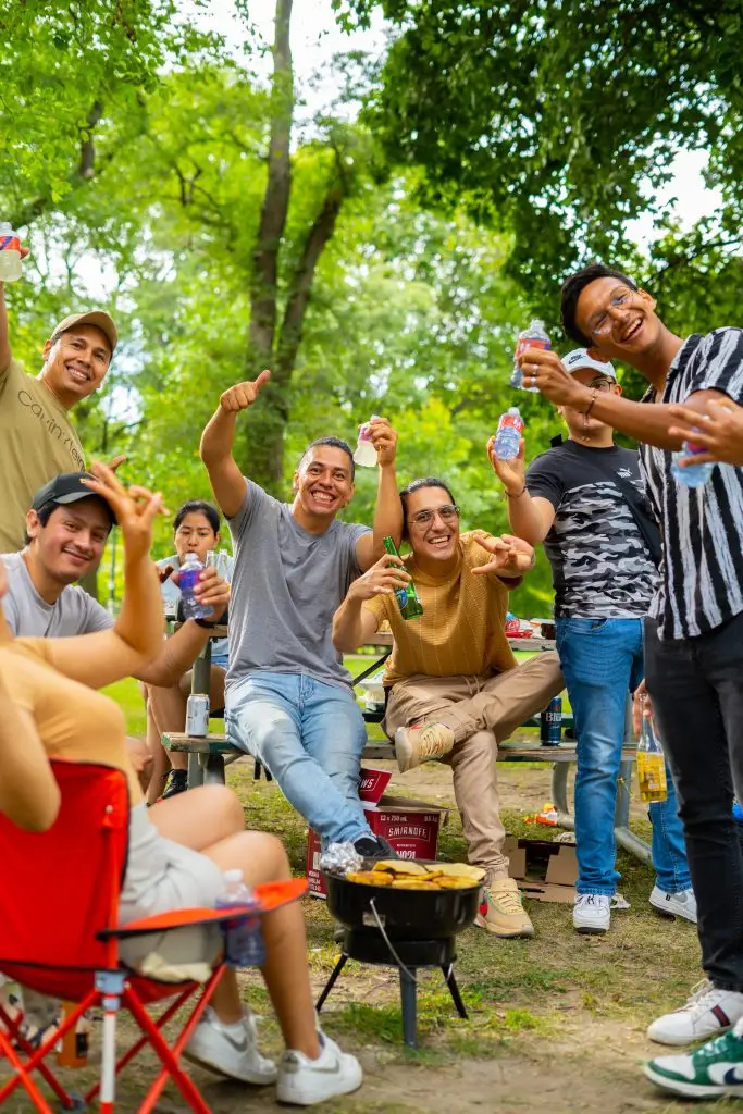 FX Productions Canada A group of people smiling and raising drinks around a small grill at an outdoor picnic in a park. Toronto Video Production Company