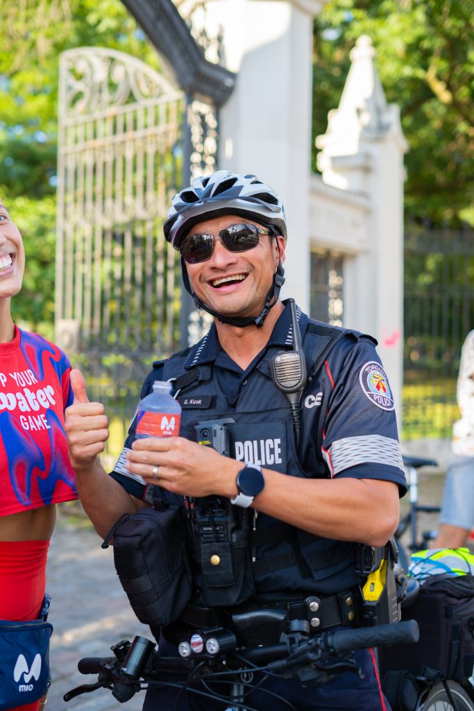 FX Productions Canada A smiling police officer in uniform and helmet gives a thumbs-up, standing outdoors near a wrought-iron gate. Toronto Video Production Company