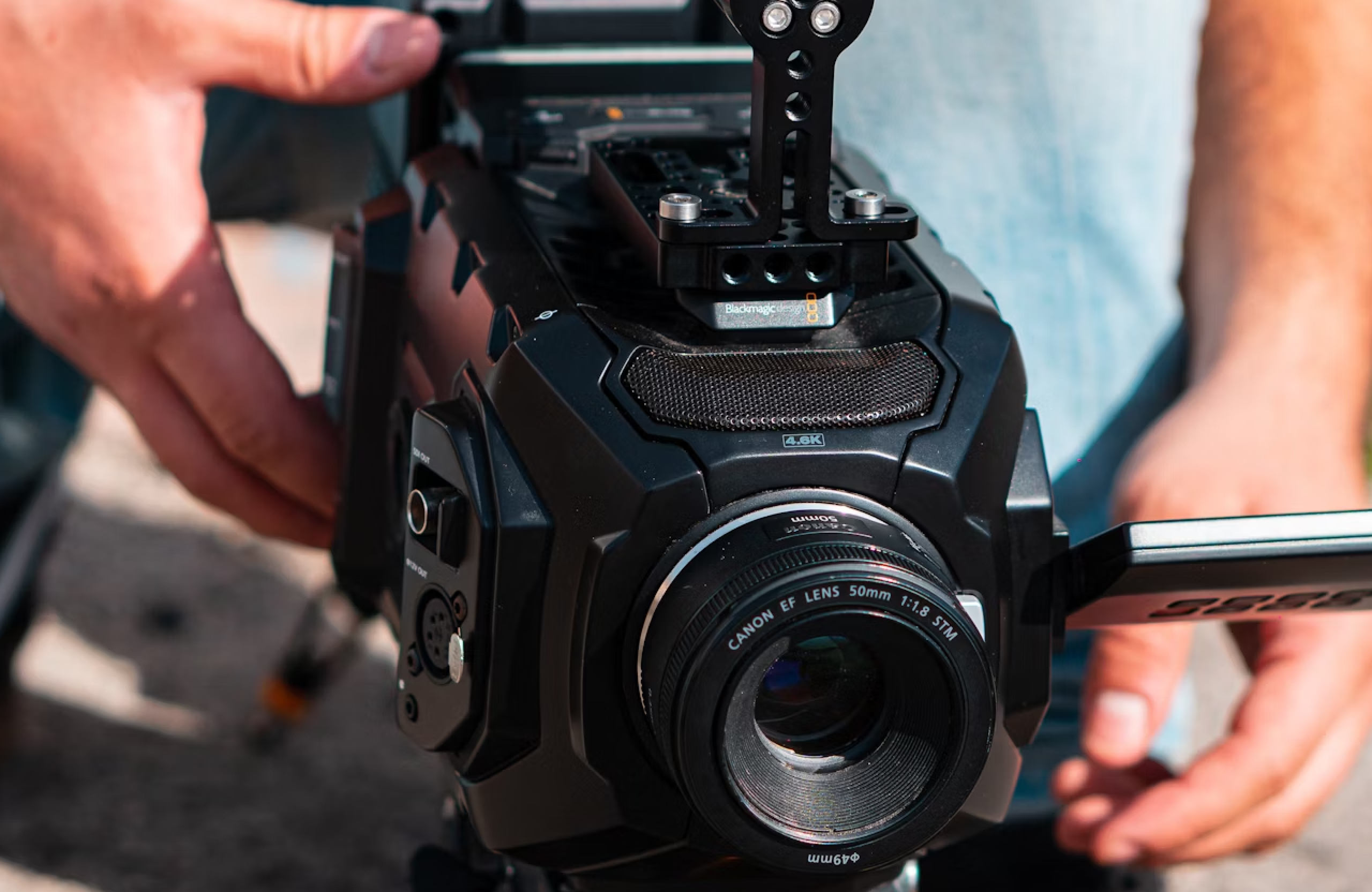 FX Productions Canada Close-up of a person's hands adjusting a professional video camera with a Canon EF lens, mounted on a tripod outdoors—capturing cinematic storytelling for a video production agency. Toronto Video Production Company