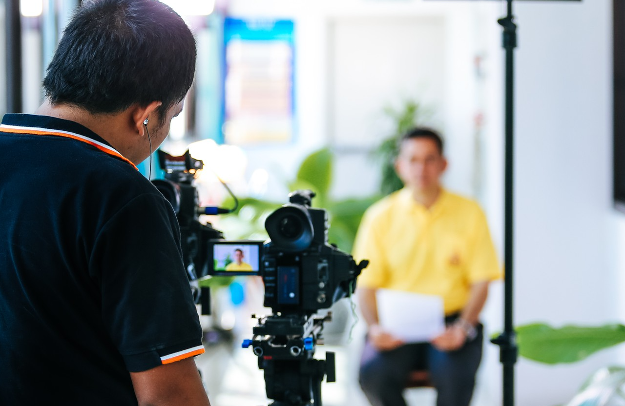 FX Productions Canada A camera operator films a person in a yellow shirt holding papers, using professional video equipment indoors—highlighting cinematic storytelling and expert video production services in Toronto. Toronto Video Production Company