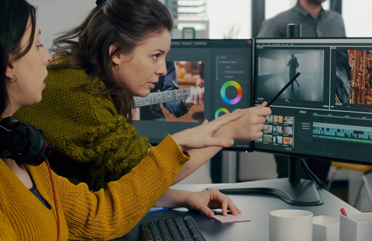 FX Productions Canada Two women work at a computer editing footage, with one pointing a pen at scenes on a dual-monitor setup in an office environment, showcasing the creative process of a video production company dedicated to cinematic storytelling. Toronto Video Production Company